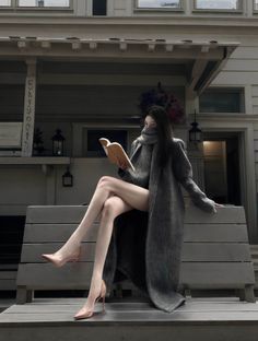 Woman in a long coat and high heels reading a book outdoors