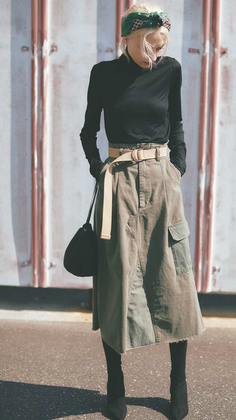 Woman with blonde hair wearing a black turtleneck, midi skirt, and headband outdoors