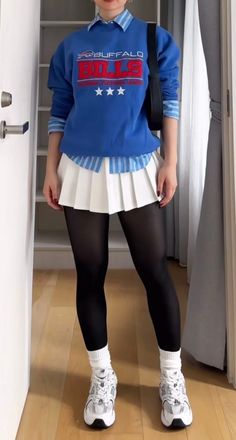 Person in a blue sweatshirt, white pleated skirt, and black tights indoors
