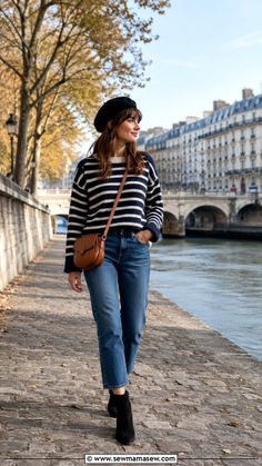 Woman in a beret and striped sweater walking along a river bank