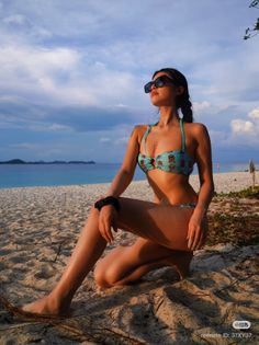 Woman in a bikini and sunglasses posing on a sandy beach at golden hour