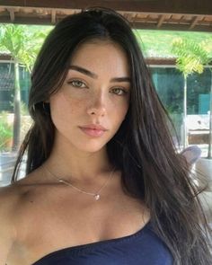 Woman with long dark hair and freckles wearing a strapless top and heart necklace