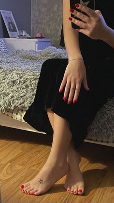 Woman with red nails and a star tattoo on her foot sitting on a bed