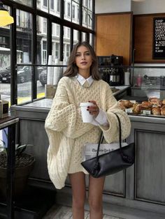 Woman in an oversized cream sweater holding a coffee cup in a cafe