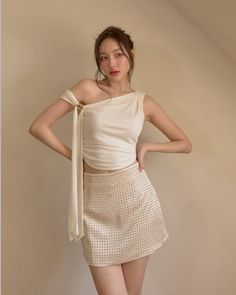 Woman in a white one-shoulder top and studded mini skirt posing indoors