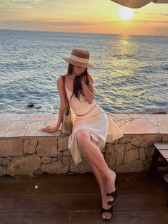 Woman in a straw hat sitting by the ocean at golden hour