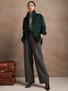 Woman in a dark green jacket and wide leg pants posing in a studio