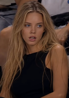 Blonde woman with blue eyes wearing a black top, looking to the side