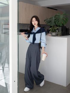 Woman in a blue shirt and wide leg pants holding a coffee cup indoors