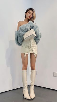 Woman in an off-shoulder top, mini skirt, and long boots posing indoors