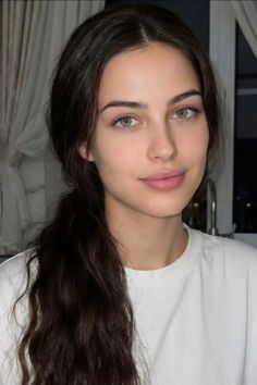 Woman with long dark hair and green eyes wearing a white t-shirt indoors