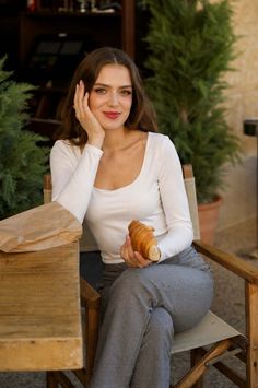 Woman with long hair holding a croissant at an outdoor cafe