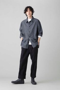 Person with curly hair wearing a denim shirt and black pants in a studio