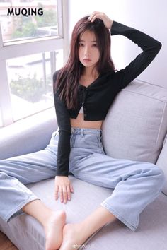Woman with long hair wearing a cropped cardigan and jeans, sitting on a sofa