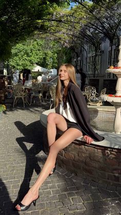 Woman in shorts and a blazer sitting outdoors at a cafe in sunlight