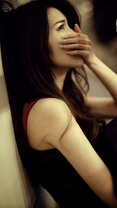 Woman with long dark hair crying with her hand covering her mouth