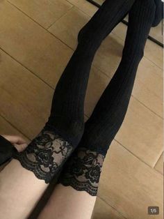 Person wearing black thigh-high socks with lace trim on a wooden floor