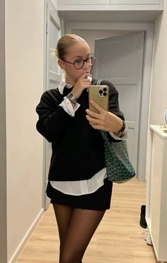 Blonde woman in glasses, black sweater, and mini skirt taking a mirror selfie