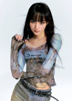 Woman with long black hair and bangs wearing a sheer top and jeans