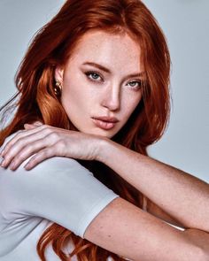 Woman with red hair and freckles wearing a white top and gold earrings