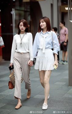 Two women holding hands and walking on a street during the daytime