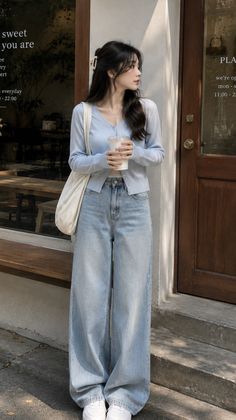 Woman in a light blue cardigan and wide leg jeans holding a drink outdoors