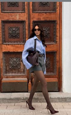 Woman in an oversized shirt, shorts, and tights walking past an ornate wooden door