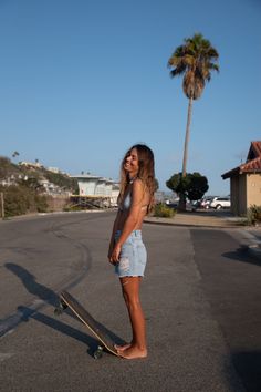 Woman in a bikini top and denim shorts standing barefoot with a skateboard