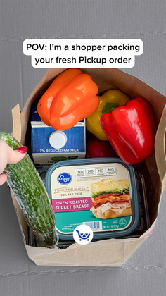 Hand placing a cucumber into a grocery bag filled with food items