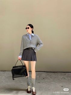 Woman in a gray cardigan and pleated skirt holding a black handbag