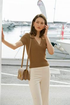 Woman in a brown top and white pants with a shoulder bag at a marina