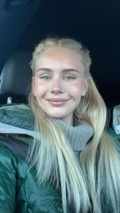 Woman with blonde hair and blue eyes wearing a green jacket and turtleneck sweater