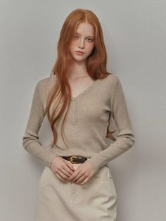 Woman with long red hair and freckles wearing a ribbed v-neck top and light pants