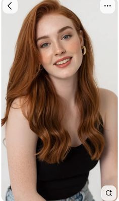 Woman with red hair and freckles wearing a black top and gold earrings