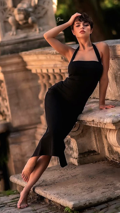 Woman in a black dress posing barefoot on a stone ledge outdoors