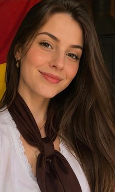 Young woman with long brown hair wearing a white shirt and brown scarf, smiling