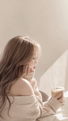 Woman with long hair in an off-shoulder sweater holding an iced coffee