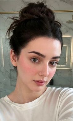 Woman with dark hair in a messy bun and natural makeup in an indoor setting