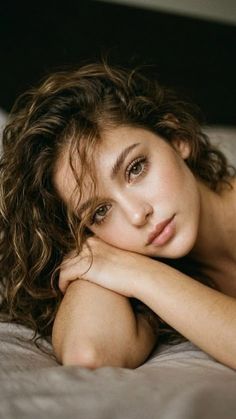 Woman with curly hair and green eyes resting her head on her arm