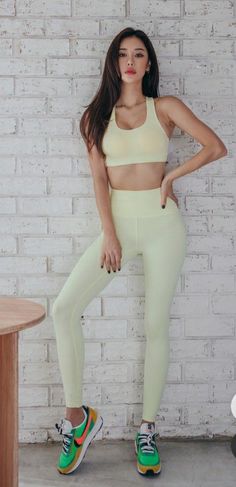 Woman in a light yellow sports bra and leggings posing against a white brick wall