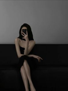 Woman in a black dress taking a mirror selfie while sitting on a couch