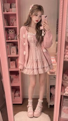 Woman in a pink dress and cardigan taking a mirror selfie in a pink room