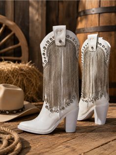White cowboy boots with rhinestone fringe and a cowboy hat on a wooden floor