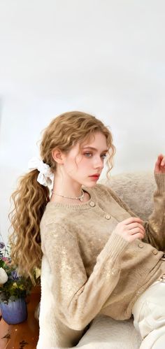 Woman with curly hair in a ponytail wearing a cardigan and necklace indoors