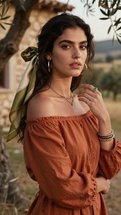 Woman with dark, wavy hair wearing an off-shoulder top and jewelry outdoors