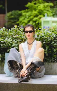 Woman in sunglasses and a sleeveless top sitting on a bench outdoors