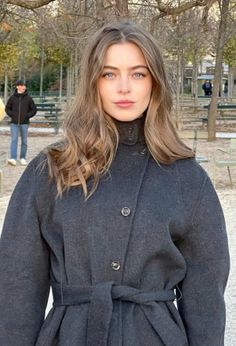 Woman with long hair and blue eyes wearing a gray coat in a park