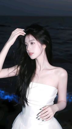 Woman with long black hair in a white strapless dress against a dark background
