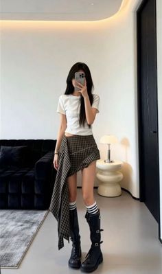 Woman in a crop top and plaid skirt taking a mirror selfie indoors