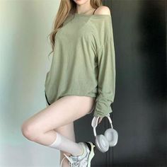 Woman in an oversized green shirt and sneakers holding headphones